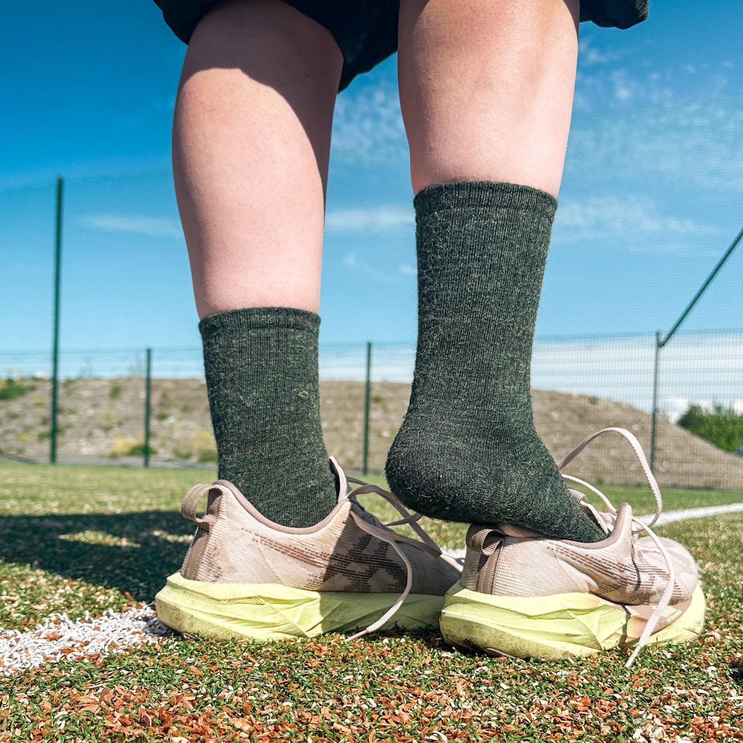 Person wearing green socks and beige sneakers on a grassy field with a clear sky.