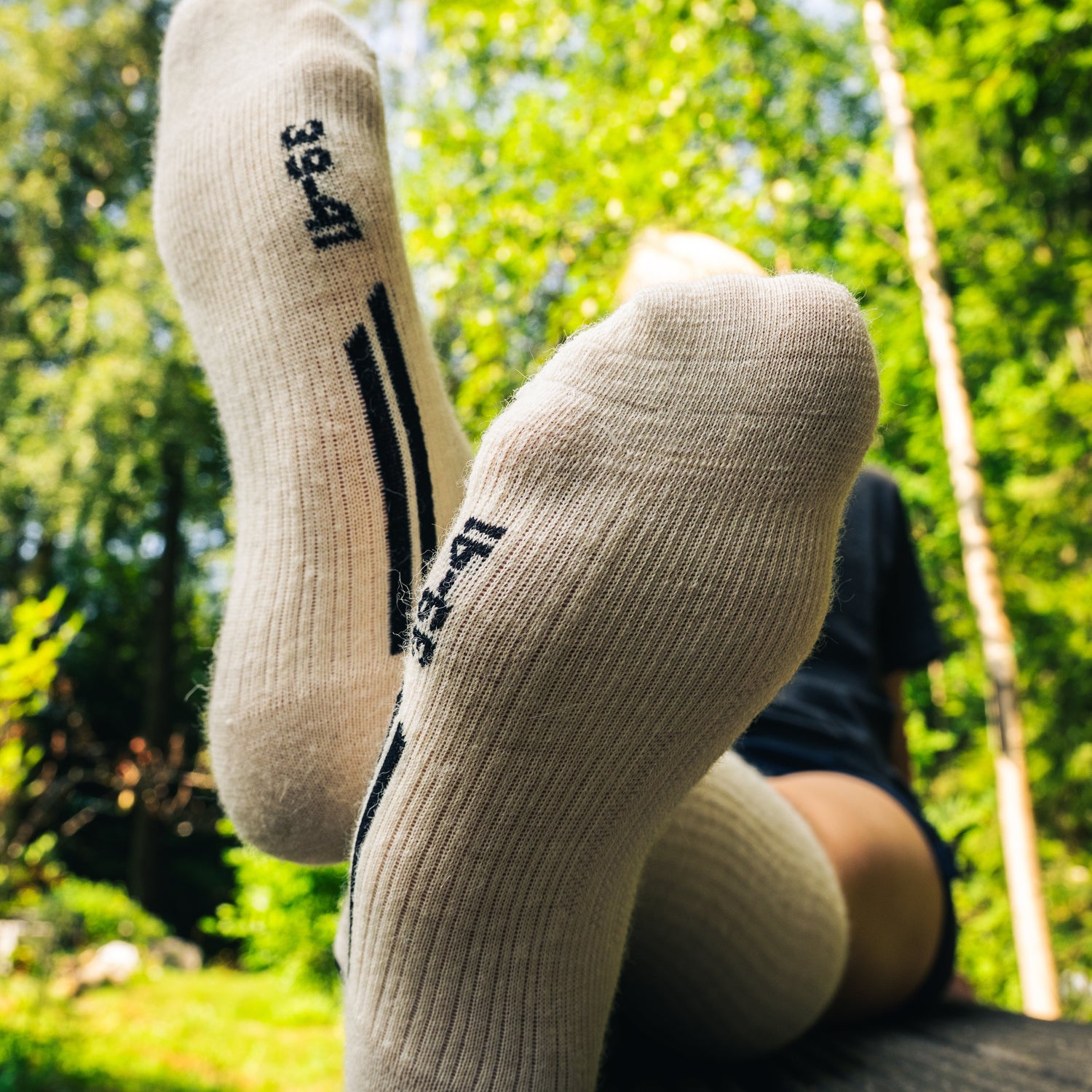 White socks with black text and design, worn by a person sitting on a swing with greenery in the background.