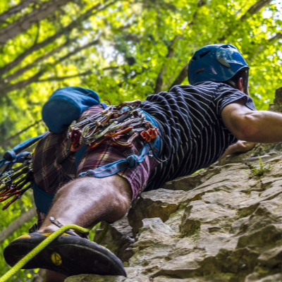 Person rock climbing with gear on a rocky surface surrounded by greenery