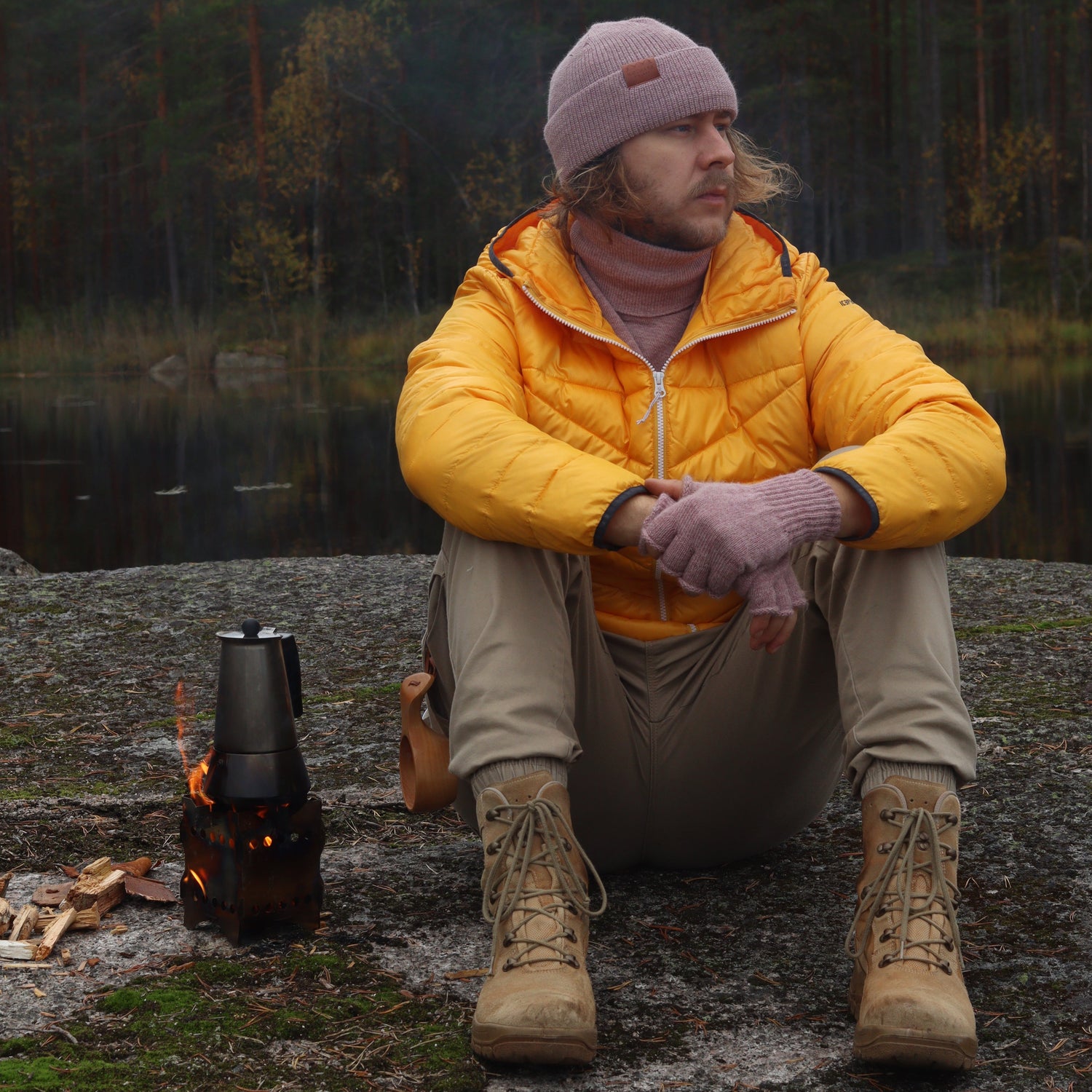 Person in a yellow jacket and purple beanie standing near a campfire in a forest setting