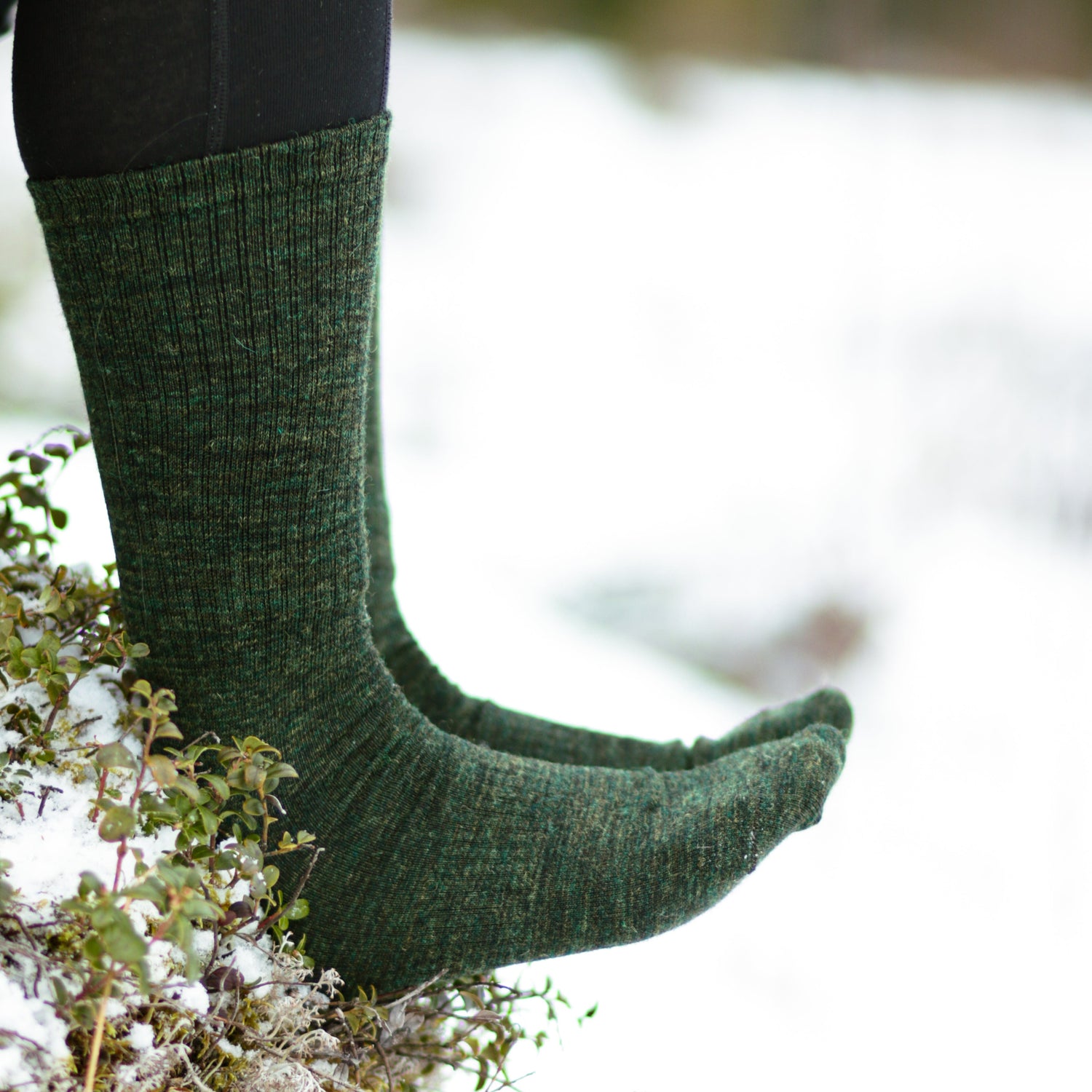 Green knitted socks worn in a snowy landscape