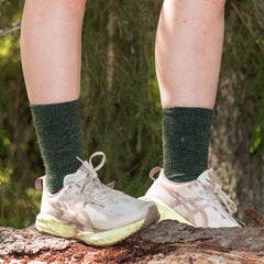 Person wearing green socks and white sneakers standing on a log with a forest background