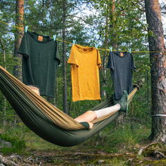 Person lying in a hammock with alpaca tee shirts hanging above in a forest setting