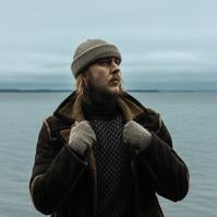 Viima alpacawool hat road grey fingerless gloves road grey worn by a man with a lake visible in the background